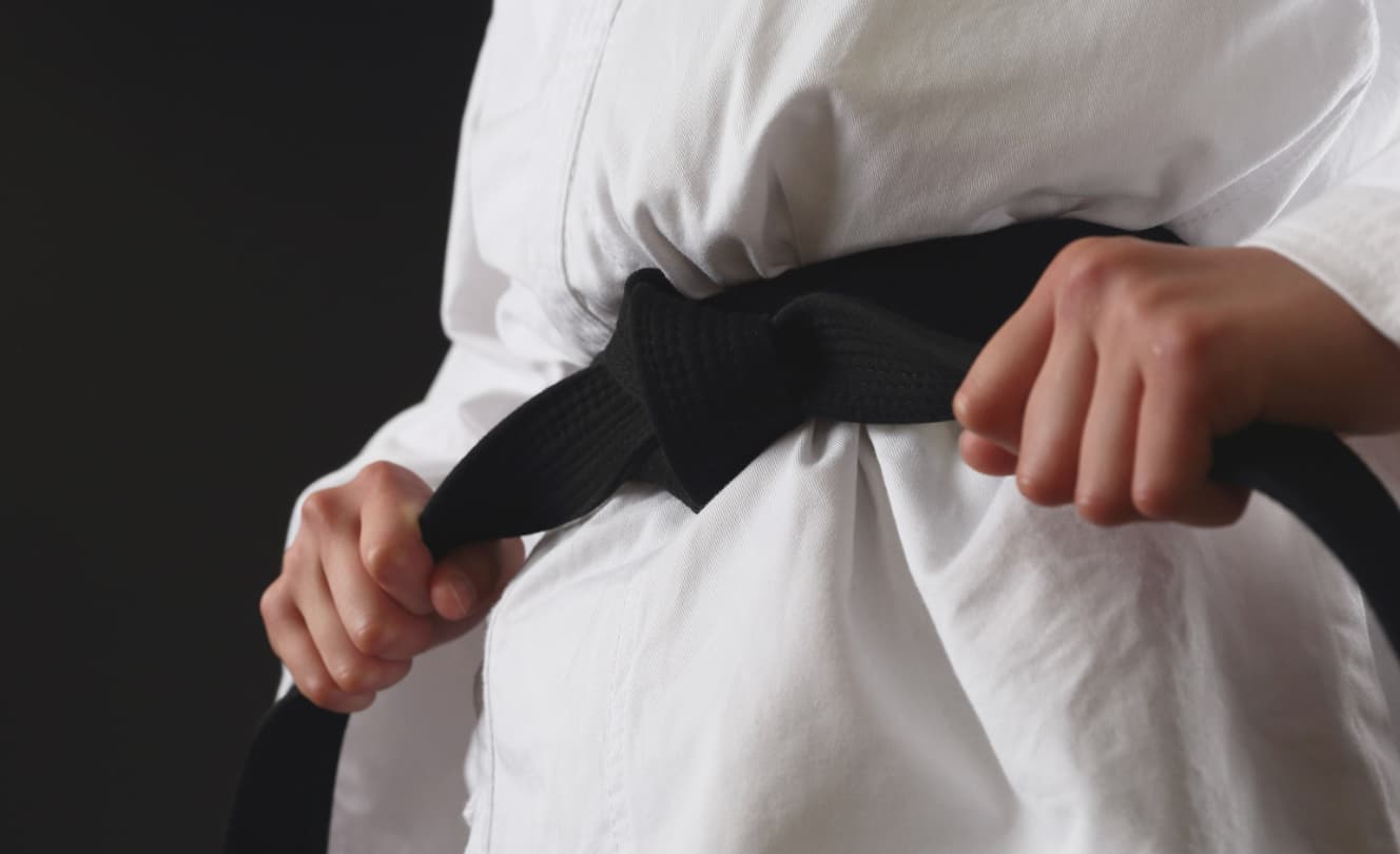 Close-up of a martial arts student tightening a black belt around a white gi.