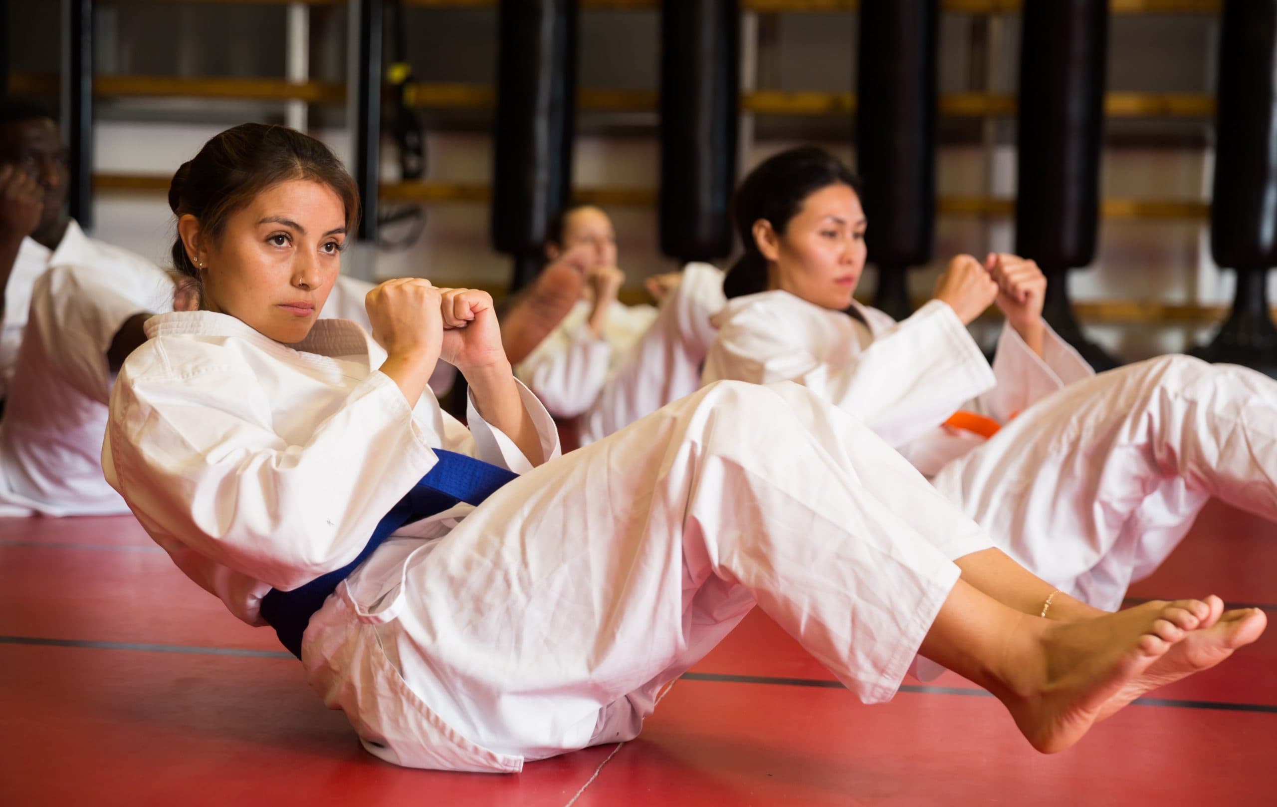 People in martial arts uniforms performing core exercises together during a dojo warm-up session.