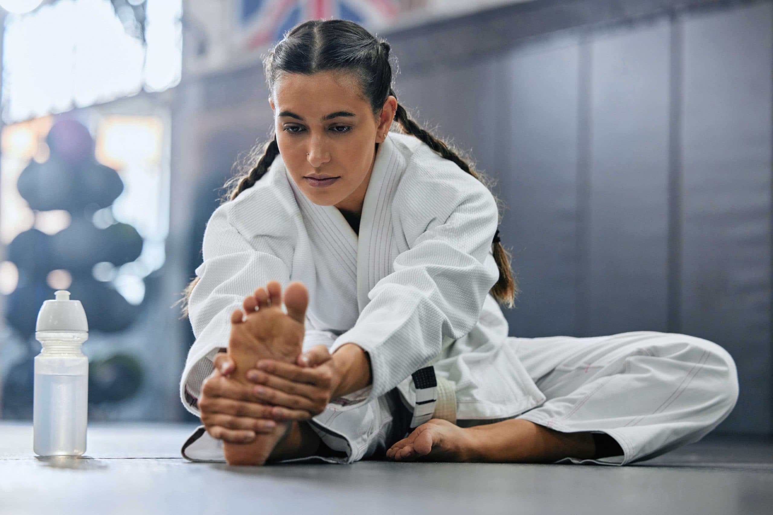 Martial arts student stretches her leg on the mat before a training session.