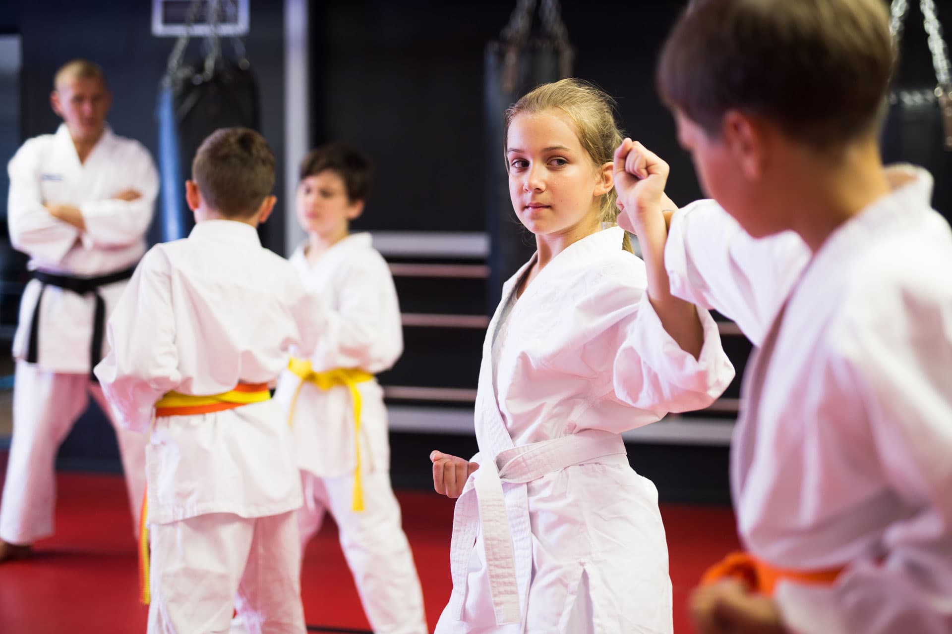 Martial arts students practice karate techniques while an instructor supervises the class in a dojo for kids.